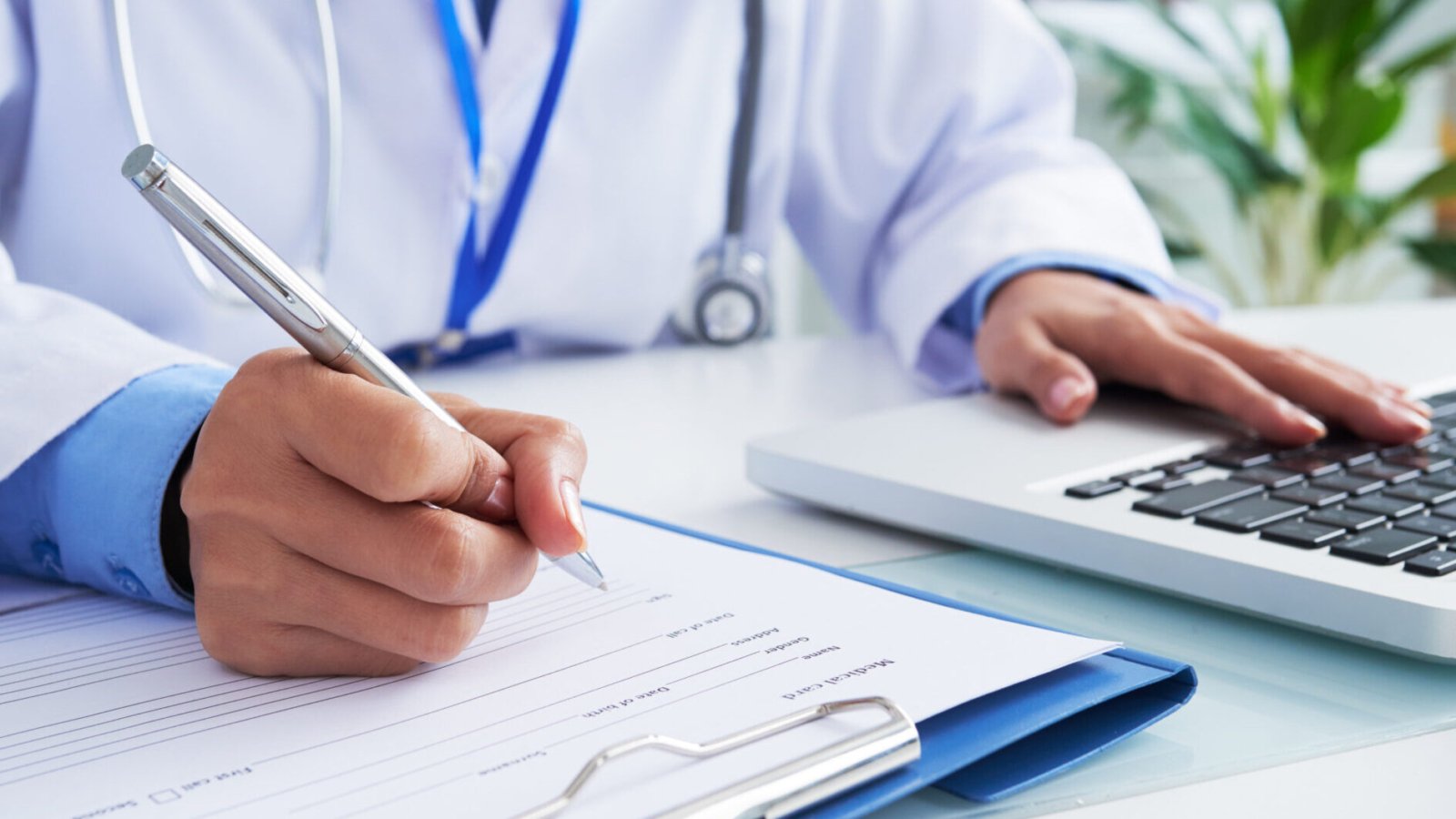 Doctor checking information in computer program before filling medical card