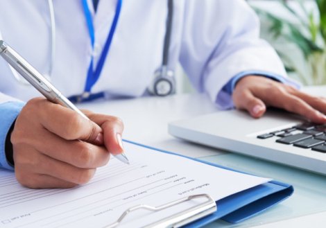 Doctor checking information in computer program before filling medical card